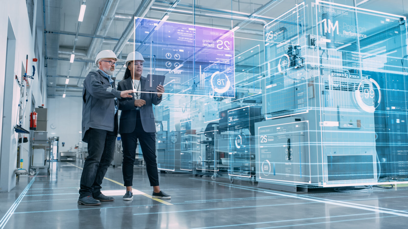 Two factory engineers in white hard hats interacting with a digital twin display and glowing HUD interface overlaid on industrial machinery.