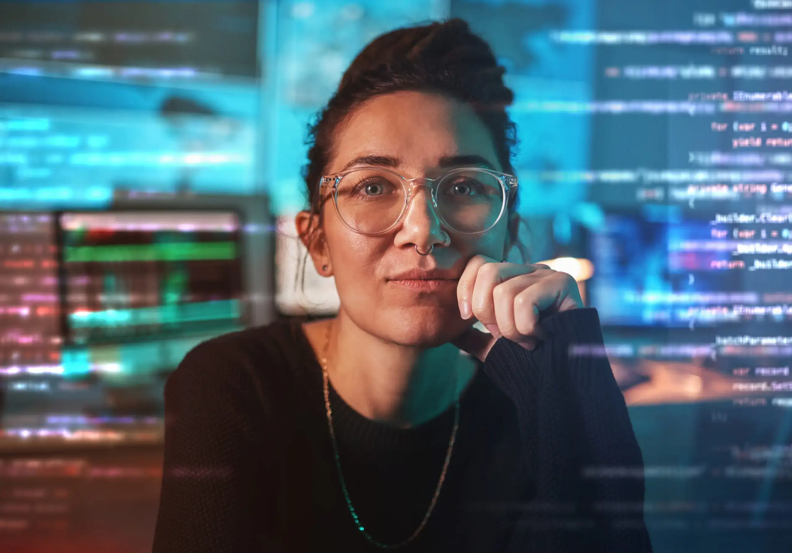 A female software developer wearing clear-framed glasses resting her chin on her hand, surrounded by glowing digital code reflections.