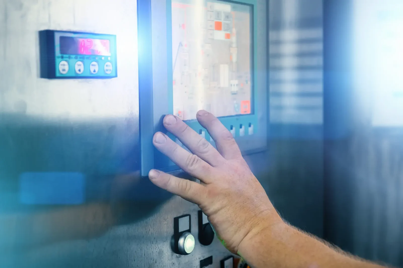 A worker's hand operating a digital touchscreen interface on an industrial machine panel alongside a digital LED read-out screen.