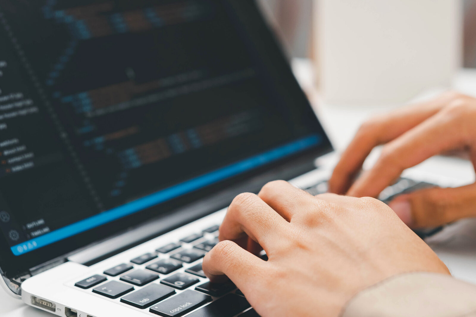 A close-up of a person's hands typing on a laptop keyboard with software code displayed on the screen.